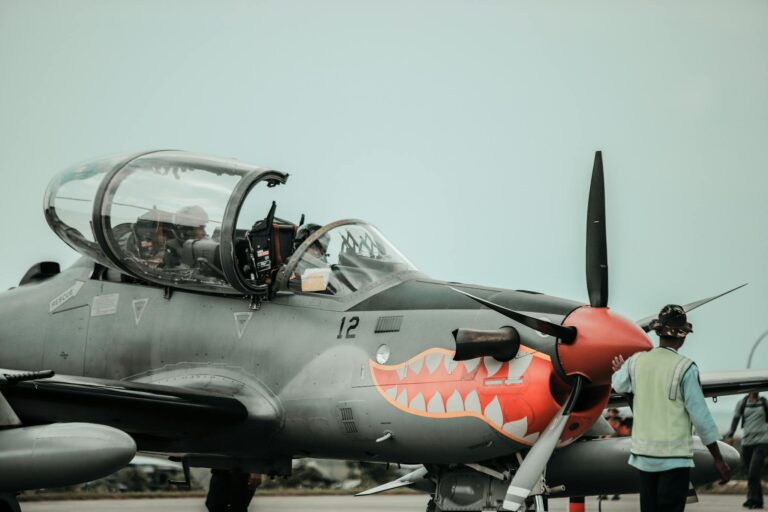 A detailed view of a military aircraft featuring shark teeth design on the runway with crew personnel.