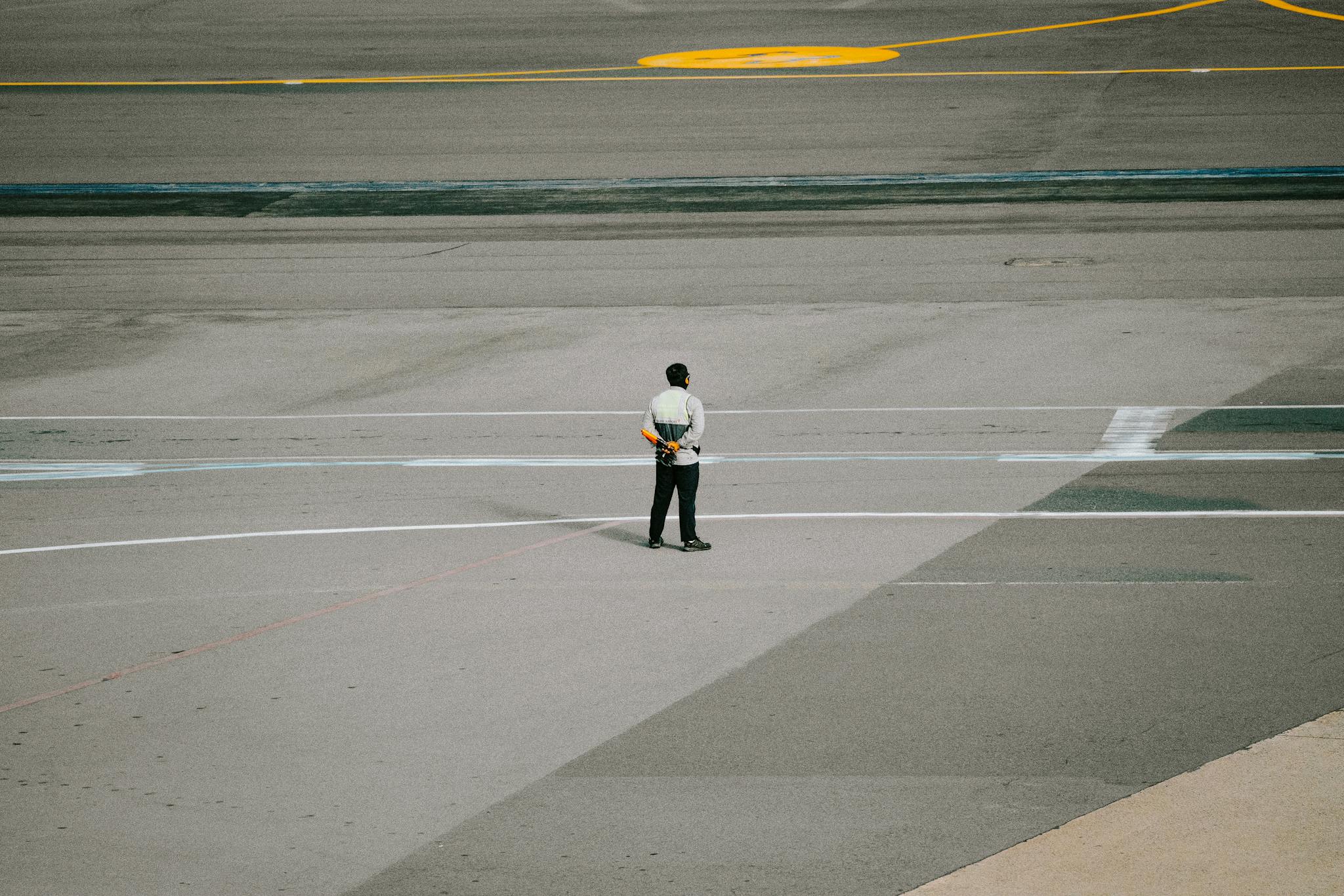 Ground staff member in uniform standing on airport runway ready for aircraft operations.