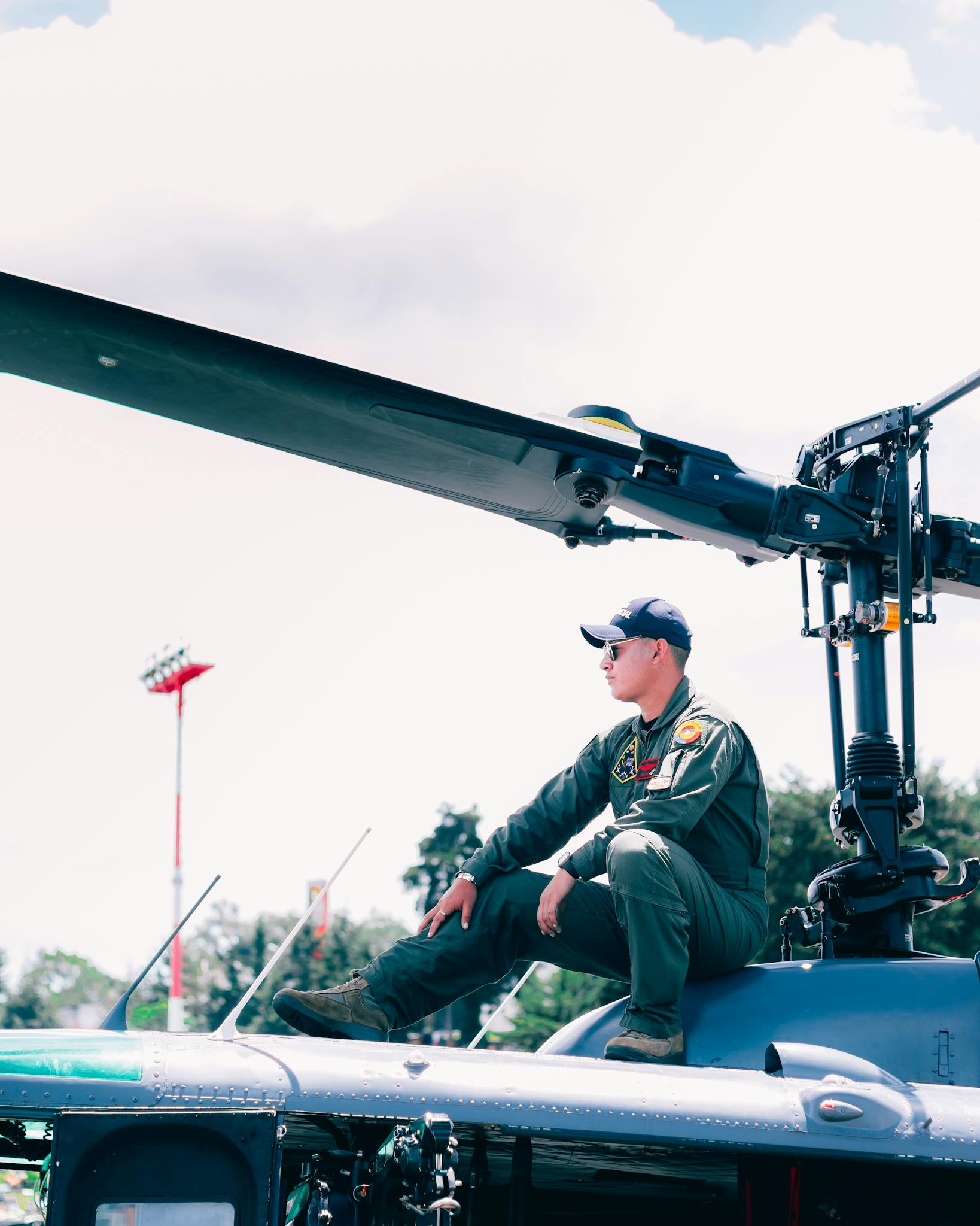 Soldier posing on helicopter with blurred outdoor background and sky in bright daylight.