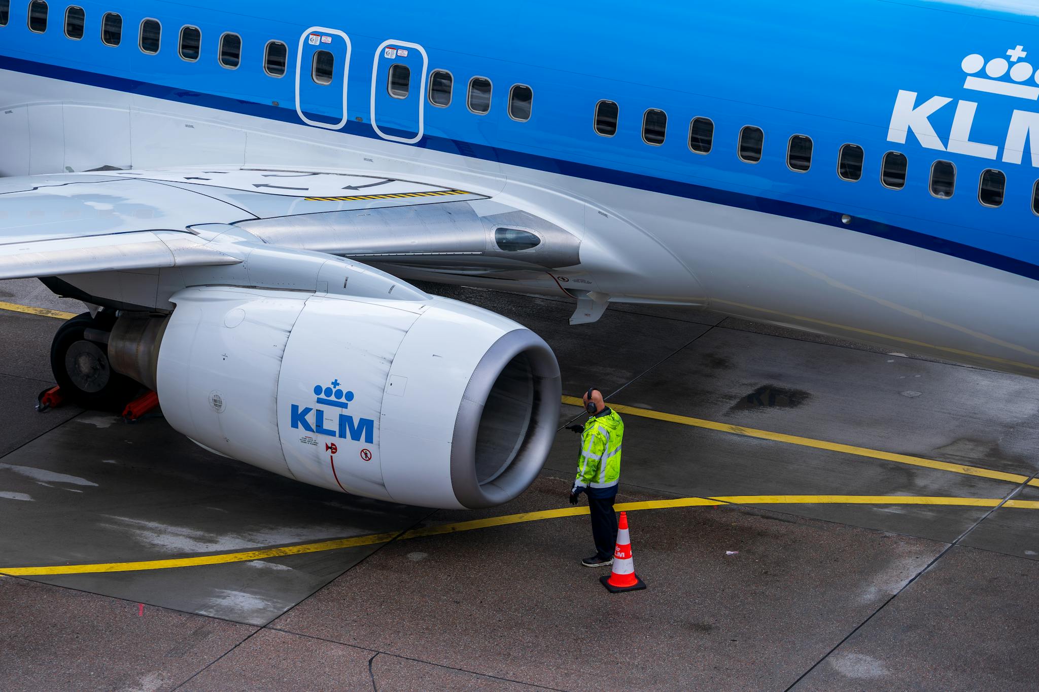 A KLM aircraft undergoing maintenance on the tarmac with an engineer inspecting it.