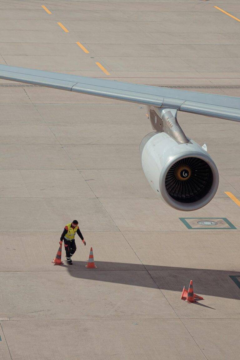 Aviation worker in safety gear checks around a parked airplane at Kloten airport.