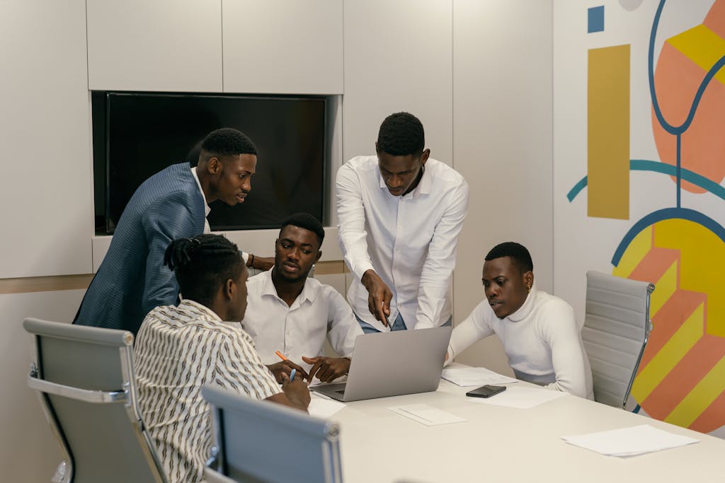 Group of diverse men in a modern office engaged in a productive meeting over a laptop.
